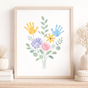 Könnte beinhalten: Ein gerahmter Aquarelldruck mit einem Blumenstrauß und Handabdrücken. Der Strauß enthält einen gelben Handabdruck, einen blauen Handabdruck, eine rosa Rose und andere bunte Blumen und Grün. Das Kunstwerk ist vor einem weißen Hintergrund.