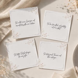 Könnte beinhalten: Vier quadratische Karten mit deutschem Text und floralen Akzenten. Die Karten sind weiß mit einem dekorativen Rand und weisen handschriftlichen Text in Schwarz auf. Die floralen Akzente sind in einer weichen, gedämpften Farbpalette gehalten. Die Karten sind auf einer neutralen Oberfläche angeordnet.