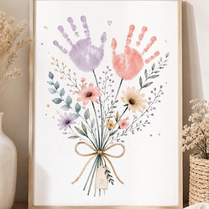 Könnte beinhalten: Ein gerahmter Aquarelldruck mit einem Blumenstrauß und zwei Handabdrücken, einer lila und einer korallenfarbenen. Der Strauß ist mit Bindfaden gebunden und enthält ein kleines Etikett mit einem Herzen. Das Kunstwerk befindet sich in einem Holzrahmen.