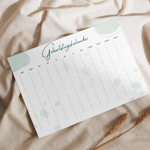 Könnte beinhalten: Ein weißer Geburtstagskalender mit dem deutschen Text "Geburtstagskalender" in Schreibschrift. Der Kalender hat Spalten für jeden Monat und Zeilen für Daten, mit hellgrünen abstrakten Formen. Der Kalender liegt auf einer beigen Stoffoberfläche.