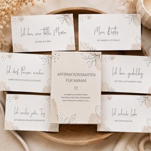 May include: A set of affirmation cards for mothers, featuring soft beige and cream tones with botanical illustrations. The cards have phrases like "I am a great mom" and "I am patient." The set includes a box with the title "Affirmation Cards for Moms."