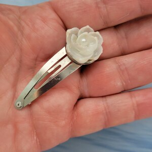 May include: A white shell flower hair clip with a pearl in the center.