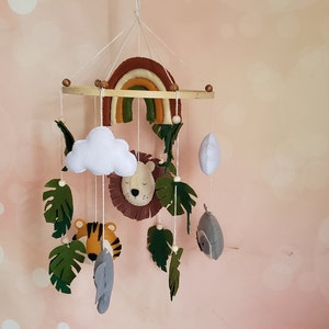 May include: A wooden baby mobile with a rainbow, cloud, lion, tiger, owl, and leaves. The mobile is made of felt and is hung from a wooden ring.