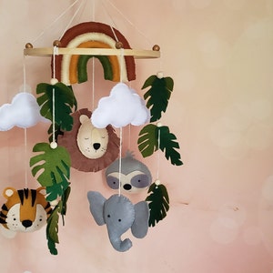 May include: A felt baby mobile with a rainbow, clouds, leaves, a lion, a sloth, an elephant, and a tiger.