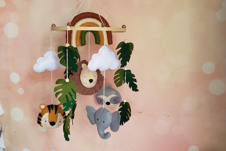 May include: A felt baby mobile with a rainbow, clouds, leaves, a lion, a sloth, an elephant, and a tiger.