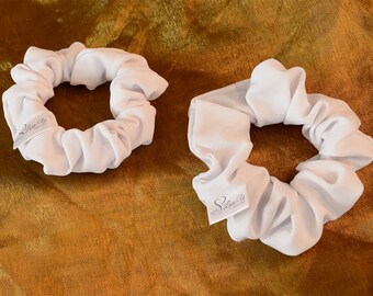 May include: Two white scrunchies with a small white tag that says "Love U" on each. The scrunchies are on a gold fabric background.