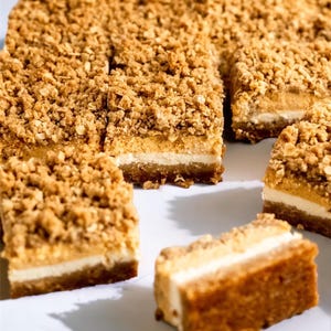 Peut inclure: Gros plan sur plusieurs barres de dessert &agrave; l'aspect superpos&eacute;. Les barres ont une base de couleur claire, une couche interm&eacute;diaire cr&eacute;meuse et une garniture dor&eacute;e et friable. Certaines barres sont coup&eacute;es en carr&eacute;s, d'autres sont enti&egrave;res.