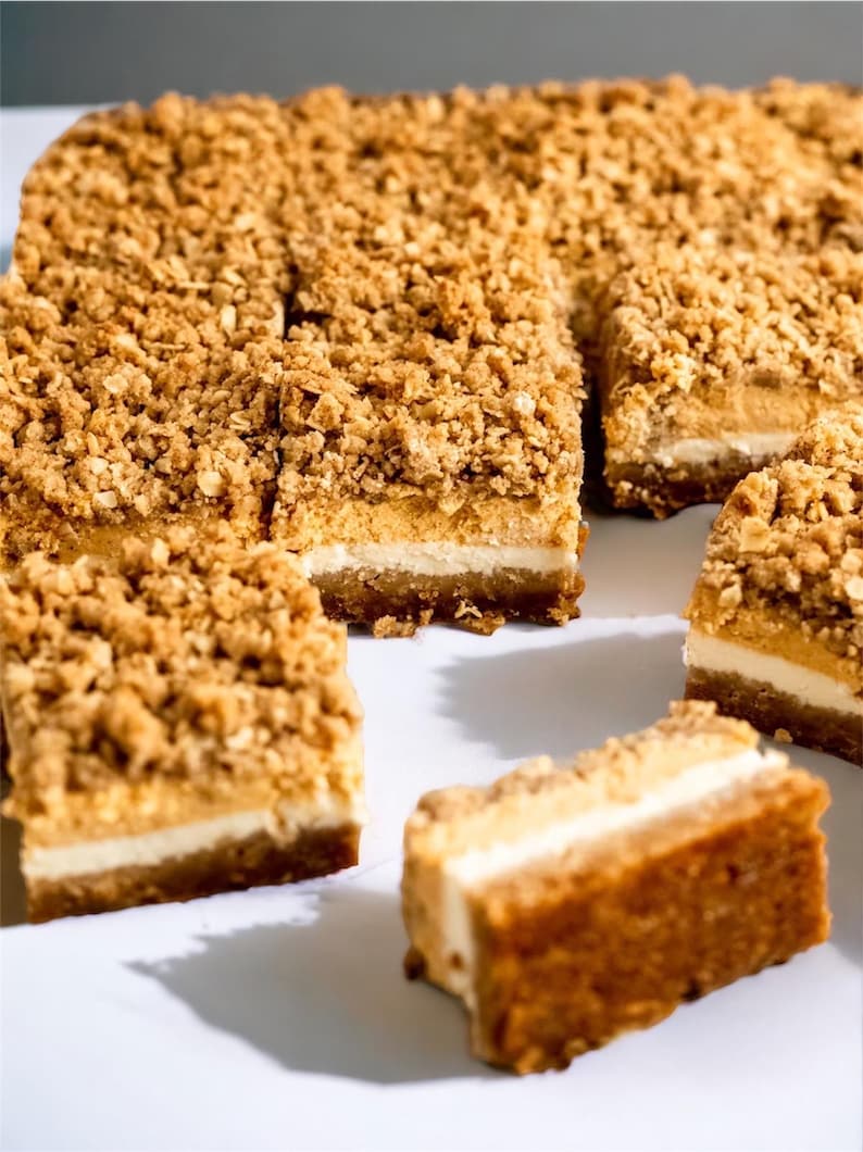 Peut inclure: Gros plan sur plusieurs barres de dessert &agrave; l'aspect superpos&eacute;. Les barres ont une base de couleur claire, une couche interm&eacute;diaire cr&eacute;meuse et une garniture dor&eacute;e et friable. Certaines barres sont coup&eacute;es en carr&eacute;s, d'autres sont enti&egrave;res.