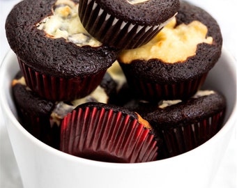 Puede incluir: Un bol blanco lleno de cupcakes de chocolate cubiertos con un remolino de glaseado blanco. Los cupcakes están en forros de cupcakes rojos.