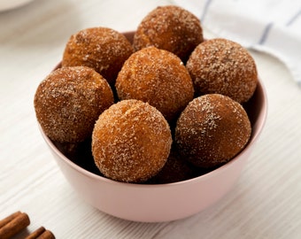 Puede incluir: Un bol rosa lleno de agujeros de rosquilla de azúcar y canela sobre una superficie de madera blanca.