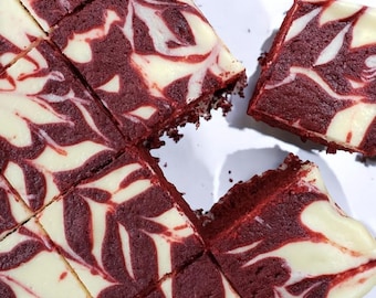 Puede incluir: Vista aérea de cuadrados de tarta de queso de terciopelo rojo con un patrón de remolino de queso crema. El postre está cortado en porciones, con algunas piezas separadas. El pastel tiene un tono rojo intenso con un patrón blanco cremoso.