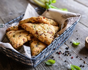 Puede incluir: Una cesta de scones salados recién horneados con hierbas y queso, sobre una mesa de madera rústica con granos de pimienta negra.