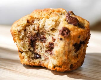 Puede incluir: Primer plano de un muffin de plátano y nueces con chispas de chocolate. El muffin está parcialmente comido, revelando la textura húmeda y desmenuzable del interior.