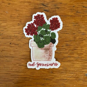 May include: A sticker of a potted red geranium plant with green leaves. The sticker has the text "red geraniums" written below the plant.