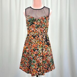 May include: A sleeveless dress featuring a black bodice with a vibrant multicolored floral print in shades of orange, red, green, and white. The upper chest area is constructed from a sheer black mesh fabric with a subtle dotted pattern.