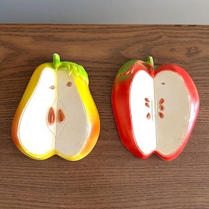 Könnte beinhalten: Eine gelbe Birne und ein roter Apfel, jeweils halbiert, werden gezeigt. Die Birne hat einen grünen Stiel und ein weißes Inneres mit braunen Kernen. Der Apfel hat einen grünen Stiel und ein weißes Inneres mit braunen Kernen. Die Früchte liegen auf einer braunen Holzoberfläche.