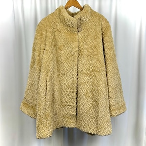 May include: A tan faux fur coat with a high collar and a single button fastening. The coat has a textured surface and long sleeves. The coat is hanging on a wooden hanger.