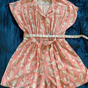 May include: A pink and white short-sleeved jumpsuit with a sailboat print. The jumpsuit has a tie waist and a button-up front. The brand name "Mallory" is visible on the collar.