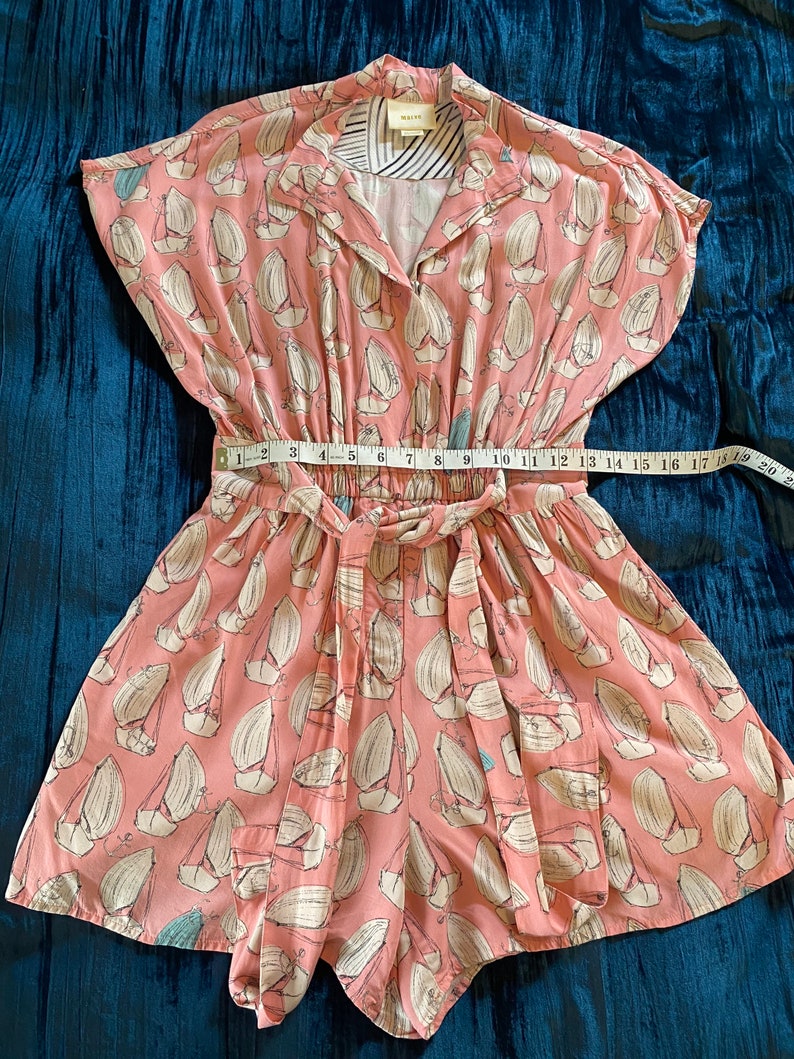 May include: A pink and white short-sleeved jumpsuit with a sailboat print. The jumpsuit has a tie waist and a button-up front. The brand name "Mallory" is visible on the collar.