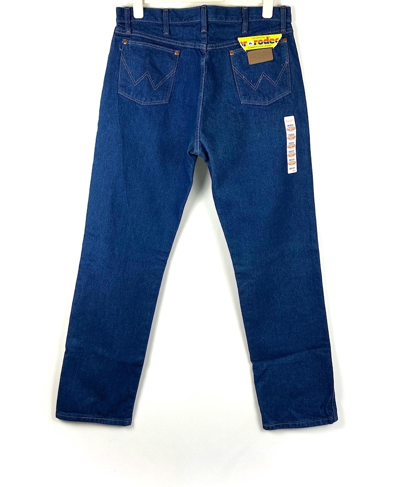 May include: A pair of dark blue denim jeans with a yellow and red Wrangler label on the back pocket.