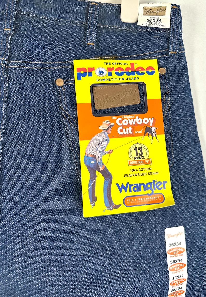 May include: A pair of blue denim jeans with a yellow and red label that says "The Official ProRodeo Competition Jeans" and "Wrangler The Original Cowboy Cut Jean". The label also features a cowboy riding a horse and a 13MWZ Original Fit logo. The jeans are size 36 x 34.