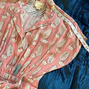 May include: A pink and white dress with a sailboat print. The dress has a button-up front and a tie at the waist. The dress is made of a lightweight fabric and has short sleeves. The dress is labeled "Malva" and has a size tag.