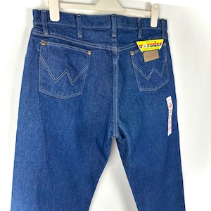 May include: A pair of blue denim jeans with a yellow and red Wrangler label attached. The jeans have a classic five-pocket style and a straight leg.