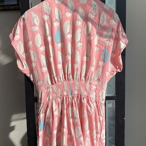 May include: A pink and white short-sleeved jumpsuit with a sailboat print. The jumpsuit has an elastic waistband and a relaxed fit.