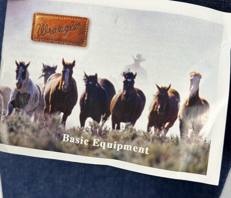 May include: A vintage Wrangler advertisement featuring a group of horses running through a field. The text "Basic Equipment" is printed below the image. The Wrangler logo is in the top left corner.