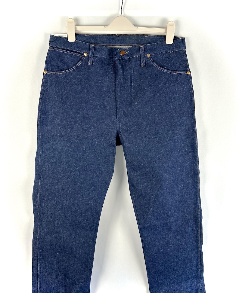 May include: A pair of dark blue denim jeans hanging on a white hanger. The jeans have a classic straight leg style and are made of a sturdy denim fabric.