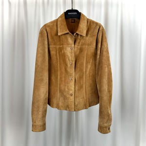 May include: A tan suede jacket with a button-up front and a collared neckline. The jacket has long sleeves and is hanging on a black hanger. The brand name "DANIER" is visible on the hanger.