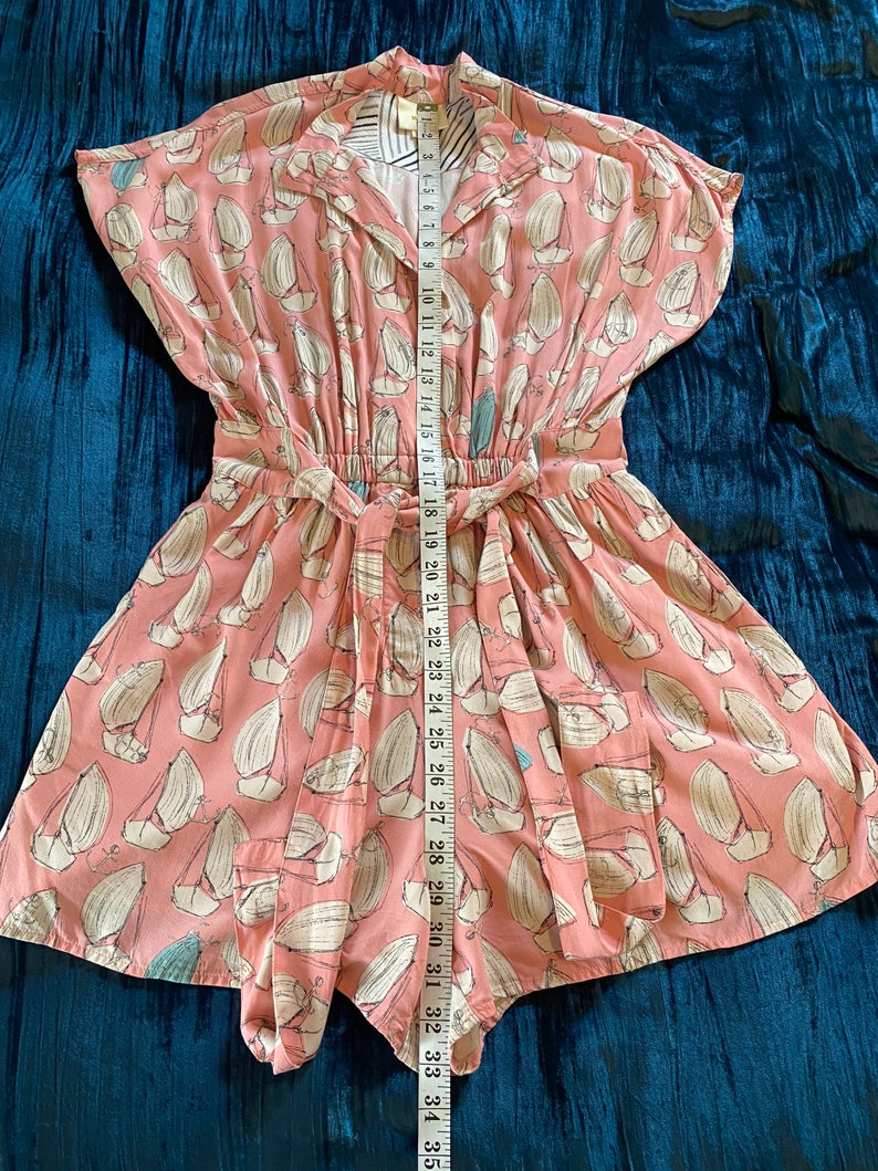 May include: A pink and white short-sleeved dress with a sailboat print. The dress has a tie at the waist and a collar.