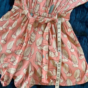 May include: A pink and white patterned short-sleeved romper with a tie waist. The romper has a sailboat print and is measured with a tape measure.