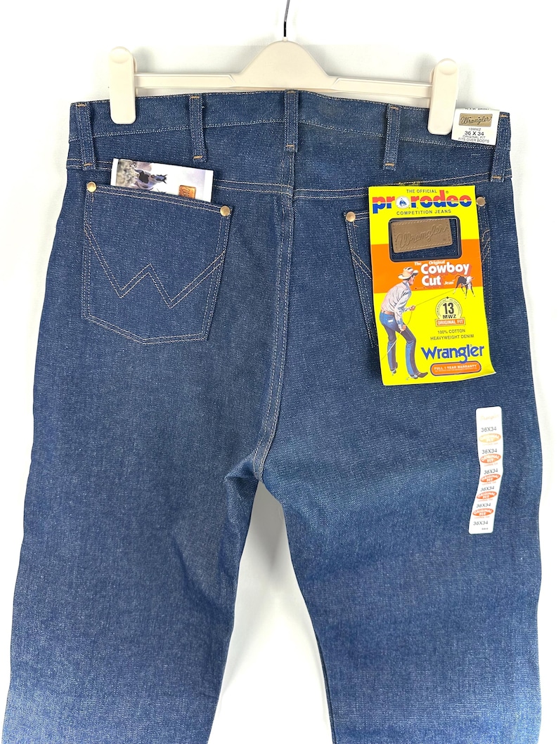 May include: A pair of blue denim jeans with a Wrangler label. The jeans are a cowboy cut and have a 'Pro Rodeo' tag attached. The tag says 'The Official Competition Jeans' and 'Cowboy Cut 13 oz.'