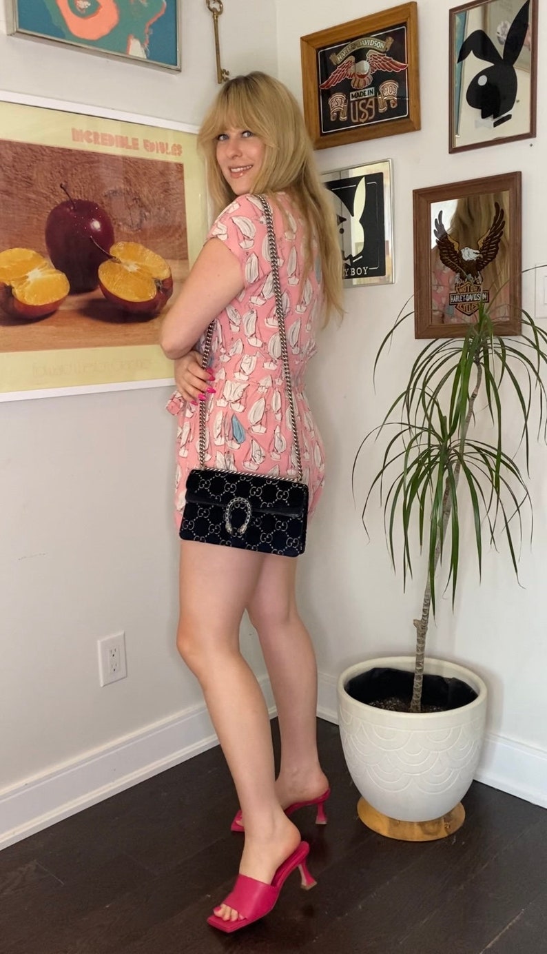 May include: A woman wearing a pink floral dress and pink heeled sandals. She is carrying a black velvet Gucci handbag with a silver chain strap and a horseshoe-shaped closure.