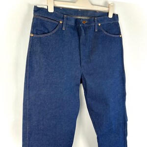 May include: A pair of dark blue denim jeans hanging on a white hanger. The jeans have a classic straight leg style and are made of a sturdy, durable fabric.