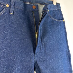 May include: A pair of dark blue denim jeans with a zipper fly and a gold zipper. The jeans have a classic five-pocket style.