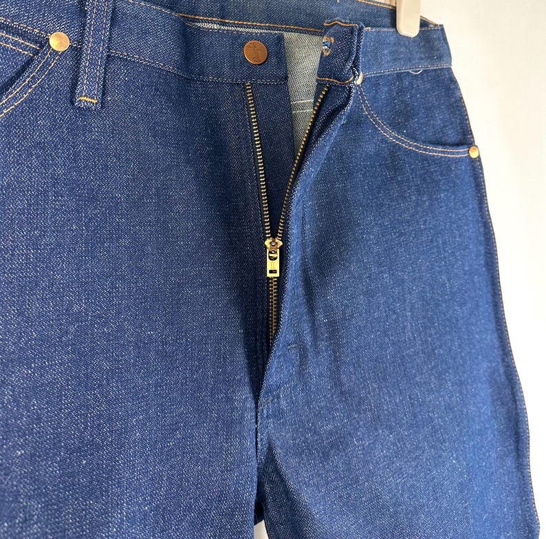 May include: A pair of dark blue denim jeans with a zipper fly and a gold zipper. The jeans have a classic five-pocket style.