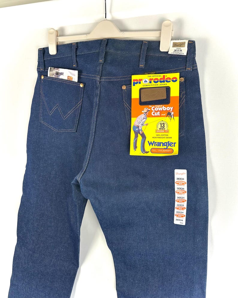 May include: A pair of blue denim jeans with a back pocket and a Wrangler label. The label says "The Official ProRodeo Competition Jeans" and "Cowboy Cut".