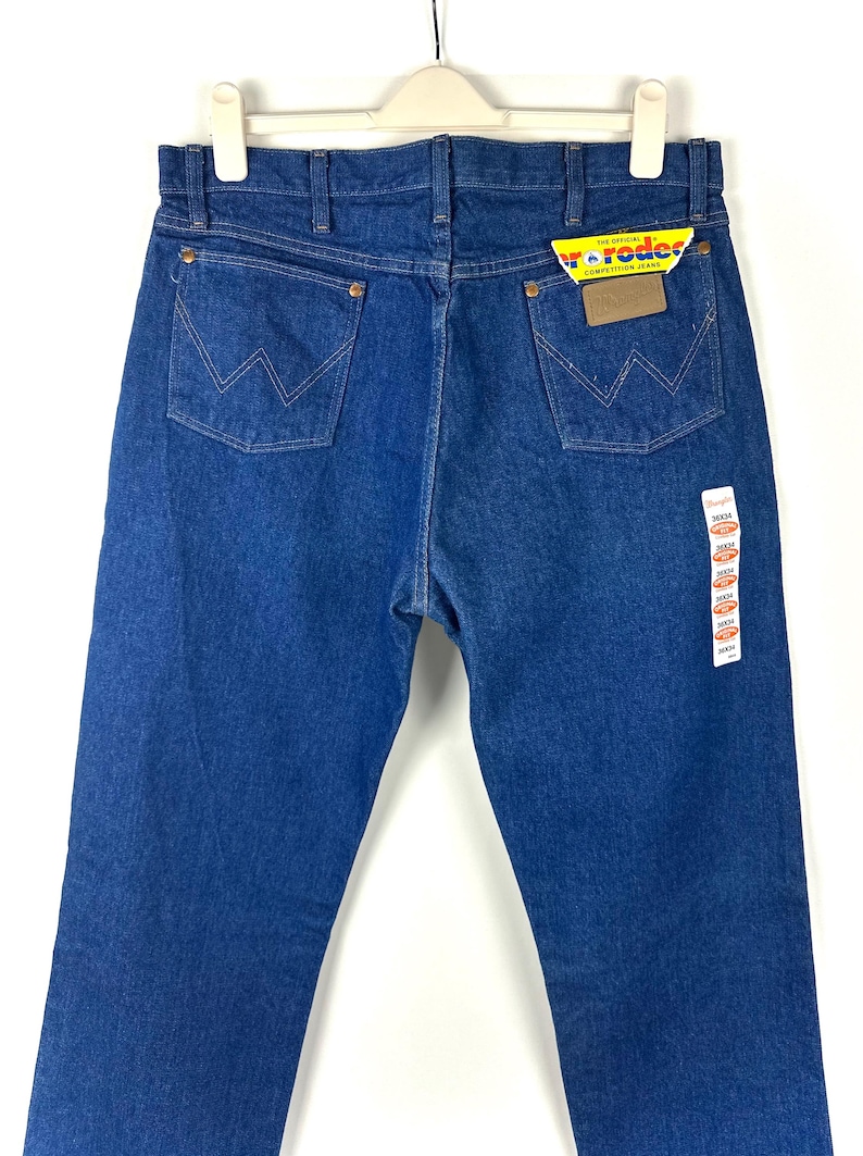 May include: A pair of blue denim jeans with a yellow and red label that says "The Official Competition Jeans" and "Wrangler".
