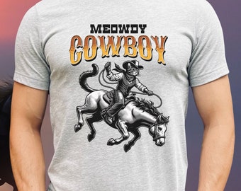May include: A gray t-shirt with a graphic of a cat wearing a cowboy hat and riding a horse. The text "MEOWDY COWBOY" is printed on the shirt.
