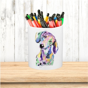 May include: White ceramic pencil holder featuring a colourful watercolour painting of a dachshund dog. The dog's name, "Emma", is written in black cursive below the image.