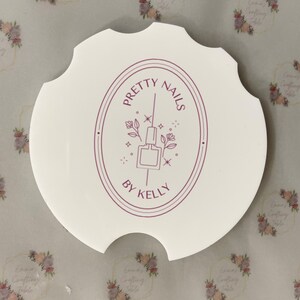May include: A white, scalloped-edge nail art palette with the text "PRETTY NAILS BY KELLY" in a burgundy oval design. The design includes a nail polish bottle and floral accents.