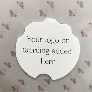May include: A white, scalloped-edge coaster with the text "Your logo or wording added here" in black. The coaster has a unique shape with a notch on one side. The background features a repeating floral pattern.