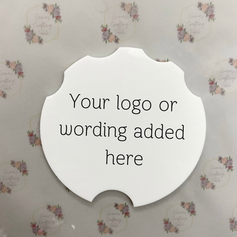 May include: A white, scalloped-edge coaster with the text "Your logo or wording added here" in black. The coaster has a unique shape with a notch on one side. The background features a repeating floral pattern.