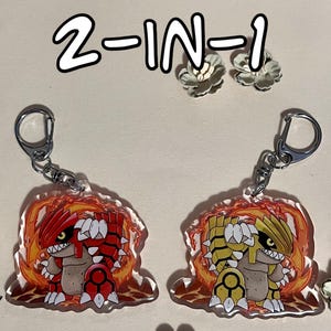 May include: Two-sided keychain featuring a cartoon character. One side shows the character in red and brown, the other in yellow and white. The text "2-IN-1" and "Normal on one side" and "Shiny on the other side" are visible.