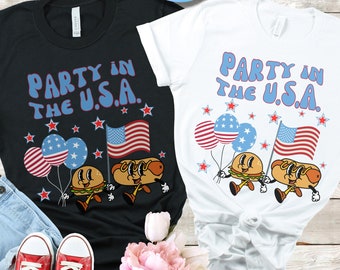 May include: Two t-shirts with a black and white design featuring a hamburger and hot dog holding American flags and balloons. The text on the shirts reads "Party in the U.S.A."
