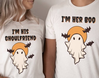 May include: A couple wearing matching white t-shirts with a ghost and moon graphic. The woman's shirt says "I'm his ghoulfriend" and the man's shirt says "I'm her boo".