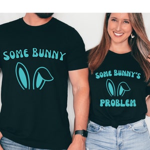 May include: Two black t-shirts with a matching design. The first shirt says "Some Bunny" with a pair of blue bunny ears. The second shirt says "Some Bunny's Problem" with a pair of blue bunny ears.