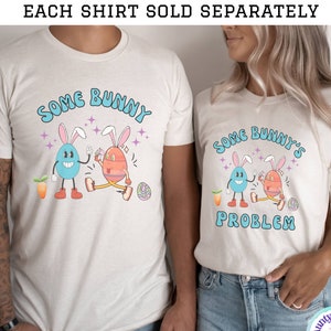 May include: Two white t-shirts with a cartoon design of two Easter eggs with bunny ears. The text on the shirts reads "Some Bunny" and "Some Bunny's Problem".